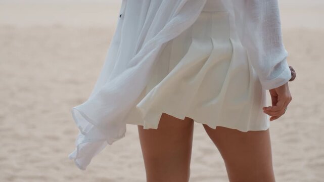 Closeup of womans pleated white skirt on sandy island beach, flowing chiffon cover, wind lifting hem, fashion model strolling along shore, sunlit texture and relaxed summer mood