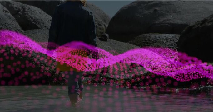 Woman wading into tidepool initiating magenta wave animation in tech overlaying jacket yellow skirt