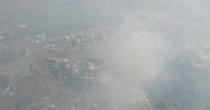 Aerial panning view. Burning rubbish causing greenhouse gas, contributor to climate change.  Extreme Poverty. People living alongside dumpsite struggling to survive through waste picking.