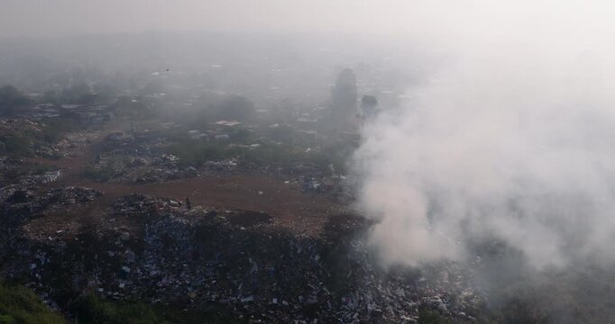 Aerial panning view. Burning rubbish causing greenhouse gas, contributor to climate change.  Extreme Poverty. People living alongside dumpsite struggling to survive through waste picking.