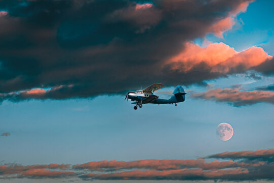 Vintage biplane flying in a dramatic sunset sky with a full moon