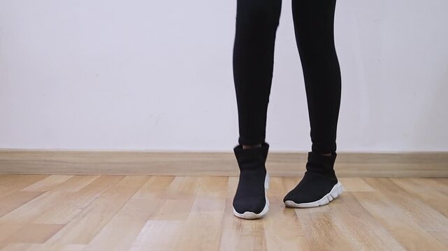 Close up of female legs in black leggings and sneakers dancing on wooden floor