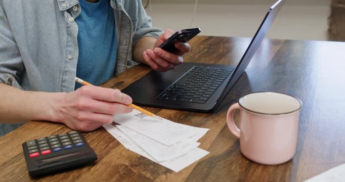Man uses smartphone to summarize utility bills as sits at laptop closeup. Male tenant plans monthly expenses budget with digital devices at home. Finances control
