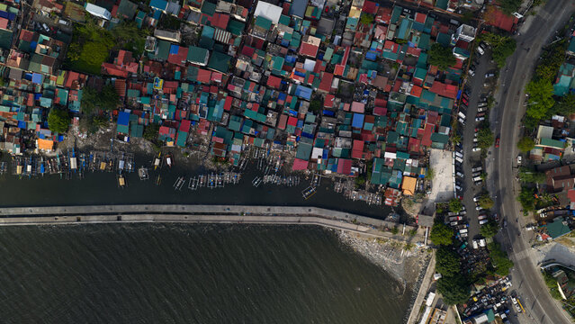 Aerial view of densely packed colorful rooftops of informal settlements along the coastline with traditional wooden boats docked by a concrete seawall Navotas, Metro Manila, Philippines.