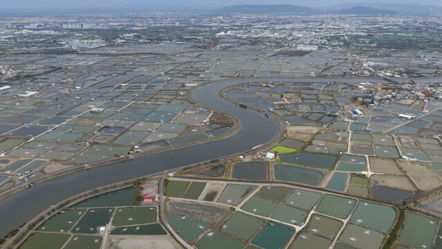 Aerial view of the Agongdian River winding through a vast grid of rectangular aquaculture ponds and shrimp farms Kaohsiung City, Taiwan.