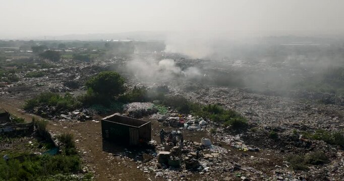 Aerial close-up fly over view. Burning rubbish causing greenhouse gas, contributor to climate change.  Extreme Poverty. People living alongside dumpsite struggling to survive through waste picking.