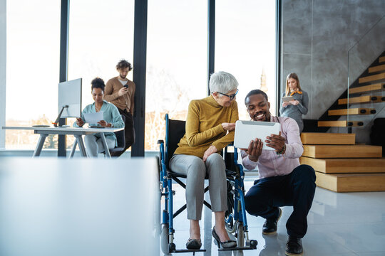 Disabled woman in wheelchair looking at computer, discussing startup project with interracial team