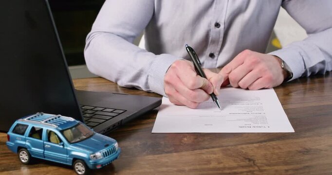 Man insurance agent fills out policy form as sits at workplace closeup. Manager prepares agreement document for client in company office. Car accident protection