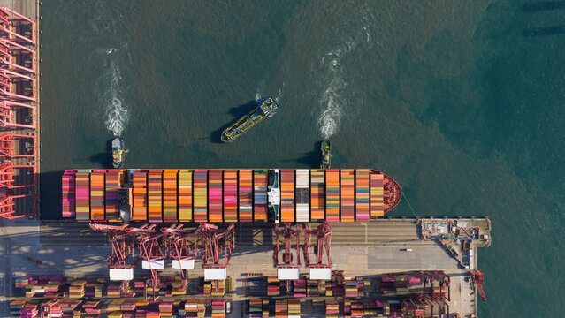 Aerial view of a large container ship docked at Kwai Tsing Container Terminal V with gantry cranes and tugboats in Hong Kong, New Territories, Hong Kong.