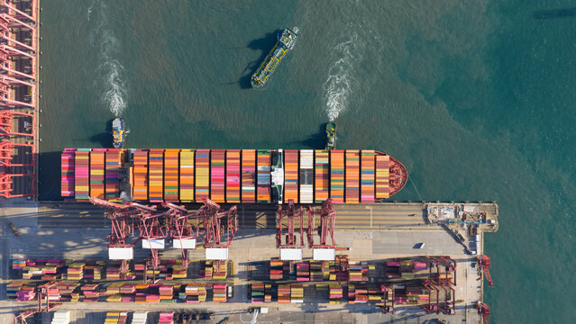 Aerial view of Kwai Tsing Container Terminal V with a large container ship docked under red gantry cranes and tugboats in the water Hong Kong, New Territories, Hong Kong.