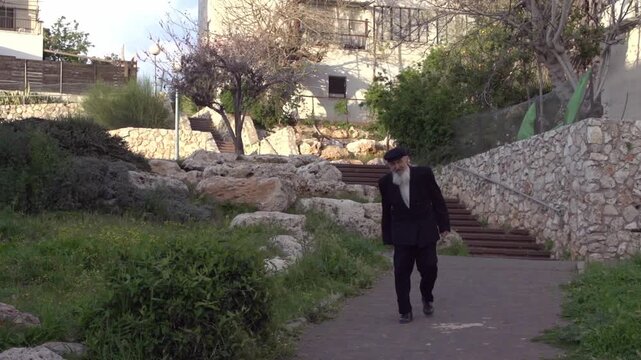 Elderly orthodox jewish man walking down a pathway in a park on a sunny day in Israel