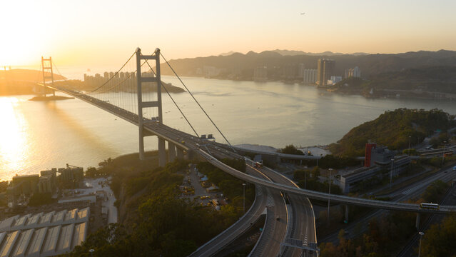 Aerial view of the Tsing Ma Bridge suspension structure spanning the water during a golden sunset with highway interchanges and distant hills in Hong Kong, China.