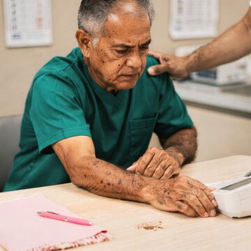 Concentrated Senior Man Checking Blood Pressure with Digital Monitor at Table with Support of Caregiver for Geriatric Healthcare and Medical Lifestyle Wellness