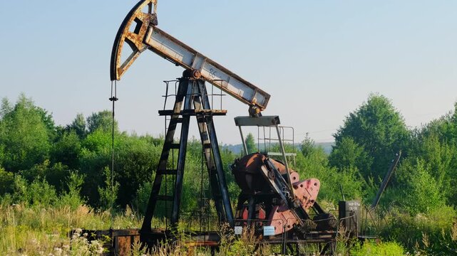 Old nodding donkey pumps crude oil from onshore well in field slow motion. Obsolete pumpjack extracts gas material from under ground at oilfield