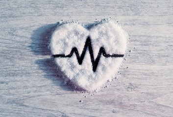 Heart shaped mound of white salt including a black pulse line on a light wooden background for heart health advocacy and salt reduction awareness campaigns