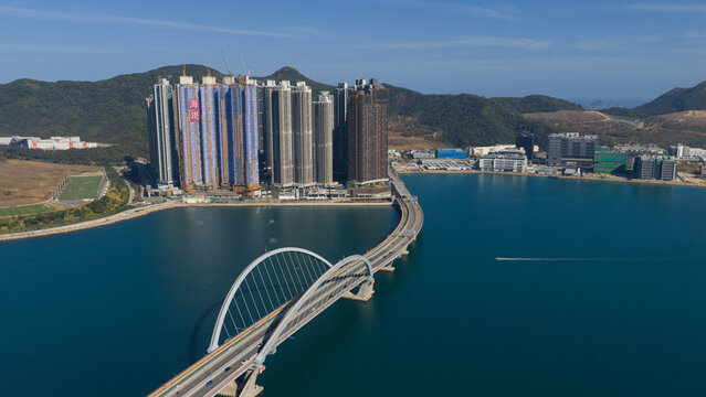 Aerial view of the Cross Bay Link bridge with its distinctive arch and modern residential skyscrapers along the waterfront in New Territories, Hong Kong.
