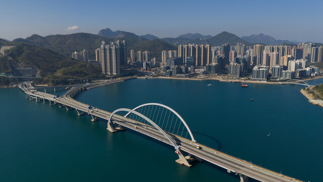 Aerial view of the Cross Bay Link bridge with its iconic double arch design spanning across Junk Bay towards the high-rise residential buildings and lush green mountains New Territories, Hong Kong.