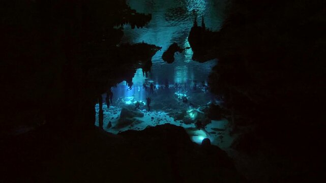 Two people move under trapped air pocket beneath cave ceiling in dim cenote cavern in Cenote Dos Ojos, Quintana Roo, Mexico