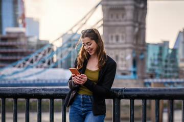 Fototapeta premium A fashionable, urban woman looks at her mobile phone in front of the city skyline of London