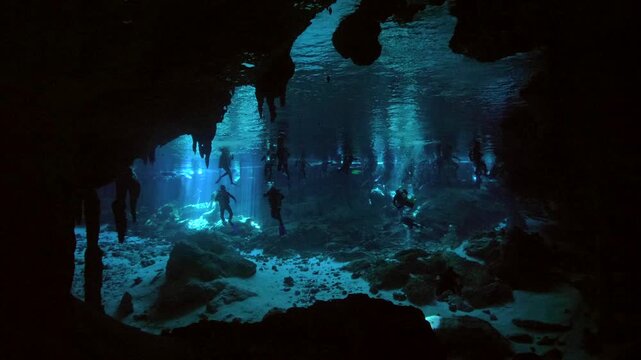 Wide composition shows diver and snorkeler beneath ceiling air space inside cenote cavern in Cenote Dos Ojos, Quintana Roo, Mexico