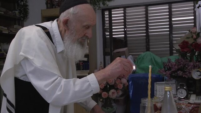 Elderly jewish man with a kippah and a tallit lighting a braided candle for the Havdalah ceremony