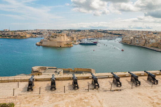 View of the cannon-lined square in Valletta, Malta, overlooking the Three Cities &ndash; Isla, Birgu, and Kalkara &ndash; with historic architecture and scenic harbor views.