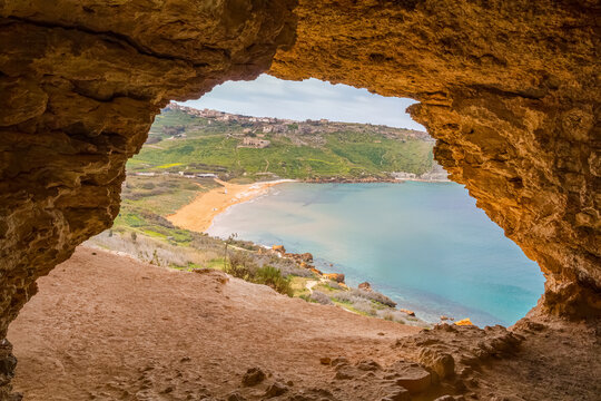 View from Tal-Mixta Cave overlooking Ramla Bay on a sunny day, panoramic vista of red sand beach, turquoise sea and rugged cliffs on Gozo Island, Malta Mediterranean landscape