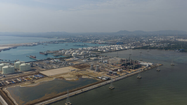 Aerial view of Map Ta Phut Industrial Estate featuring numerous oil storage tanks, refinery facilities, and a coastal harbor under a hazy sky Map Ta Phut, Rayong, Thailand.