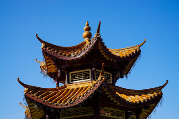 Fototapeta premium Detailed view of a traditional Chinese pagoda with ornate curved roofs and ceramic tiles under a clear blue sky, ideal for travel, culture, and architectural design use.