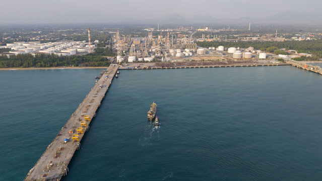 Aerial view of the Map Ta Phut industrial port featuring a long pier, storage tanks, and a ship in the water Map Ta Phut Energy terminal, Rayong, Thailand.