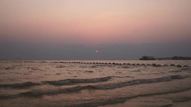 Scenic view of waves lapping on the shore with a line of buoys and tourist boats at twilight.