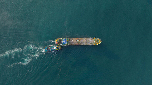 Aerial view of a large tanker ship being assisted by a tugboat in the turquoise waters of the Gulf of Thailand near Map Ta Phut Energy terminal, Rayong, Thailand.