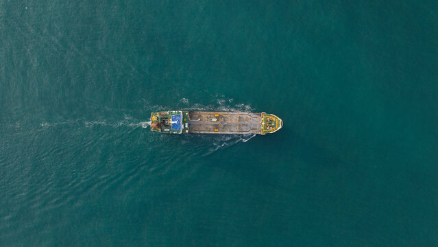 Aerial view of a large cargo ship cruising through deep turquoise waters with a white wake in Map Ta Phut Energy terminal, Rayong, Thailand.