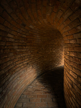 Curved brick tunnel in dim light with a winding path and soft shadows