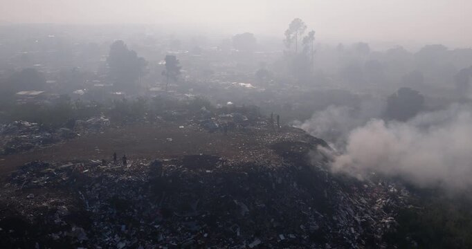 Aerial close-up panning view. Burning rubbish causing greenhouse gas, contributor to climate change.  Extreme Poverty. People living alongside dumpsite struggling to survive through waste picking.