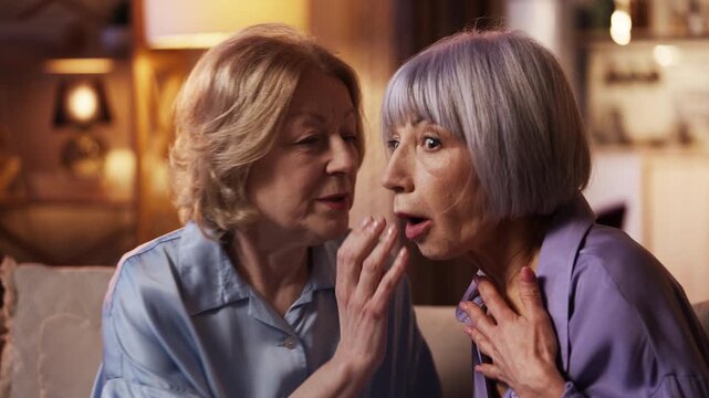 Senior woman sharing secrets with surprised female friend, warm companionship