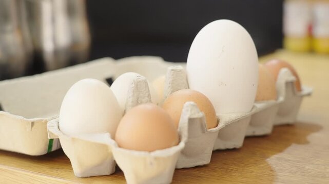 Long shot of a egg box in kitchen with a single large egg standing out