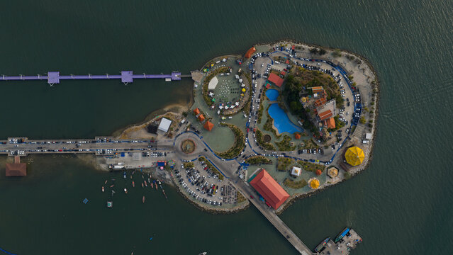 Aerial view of Koh Loi island featuring the Wat Ko Loi temple, parking areas, and a blue swimming pool surrounded by the sea in Si Racha, Chon Buri, Thailand.