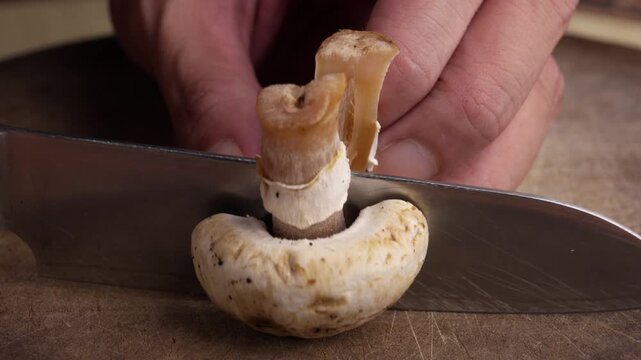 Close-up of a fresh champignon mushroom being sliced with a knife on a cutting board, revealing both halves during food preparation in a clean kitchen setting
