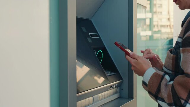 Close-up of female hands using smartphone for contactless payment at an atm to withdraw money, concept convenience of nfc technology for modern electronic banking and finance