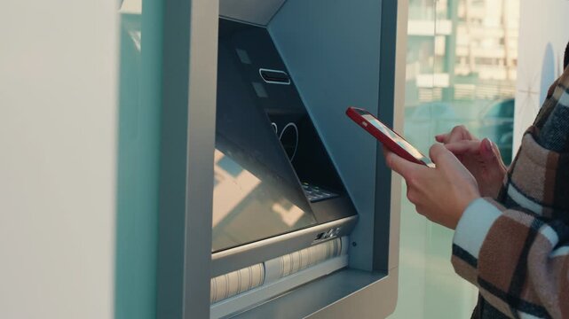 Woman using smartphone for contactless cash withdrawal at atm. Cardless technology for secure payment, nfc banking transaction, and convenient financial services on street