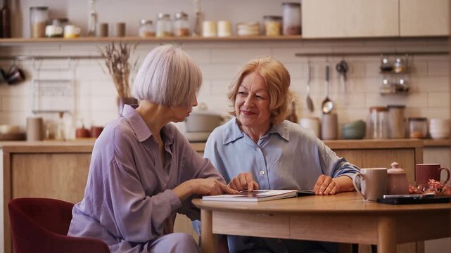 Positive senior women looking through photo album, sharing joyful memories