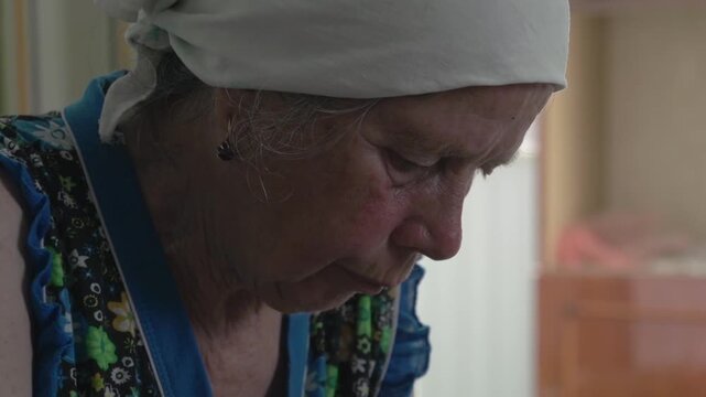 Profile view of a concentrated senior woman wearing a headscarf working hard at home