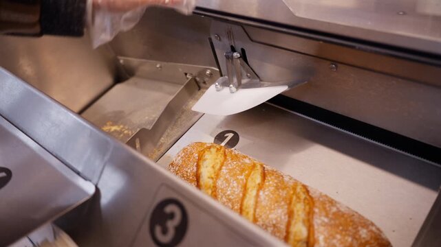 Self service bread slicer machine in grocery store, customer hand in disposable glove placing fresh baguette for automatic cutting. Food retail, hygiene, bakery technology and shopping concept.