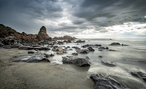 Rocky coast, rocks on the beach, dark rain clouds, long time exposure, West Coast, South Island, New Zealand