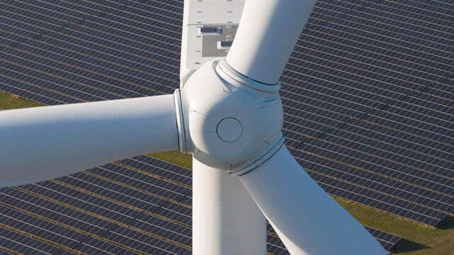 Aerial view of a white wind turbine hub and blades positioned over a large array of solar panels.