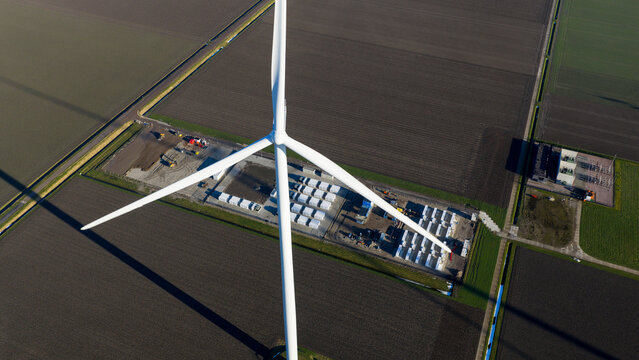 Aerial view of Windplan Groen wind turbine and battery storage facility surrounded by agricultural fields in Dronten, Flevoland, Netherlands.
