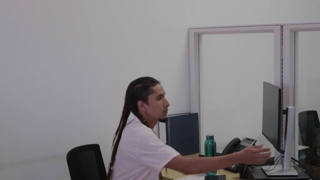 Young man with dreadlocks sitting at his desk, turning on the computer and starting to work