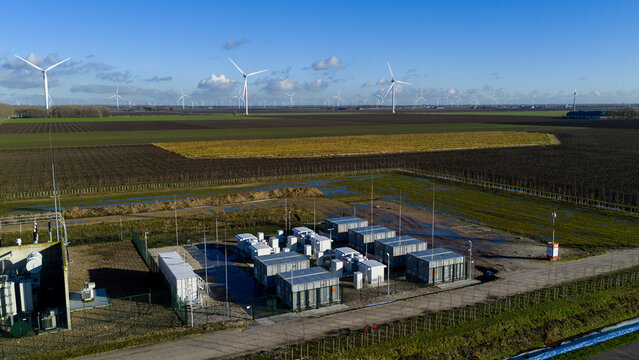 Aerial view of the Windplan Groen battery storage facility and wind turbines across flat agricultural fields in Dronten, Flevoland, Netherlands.