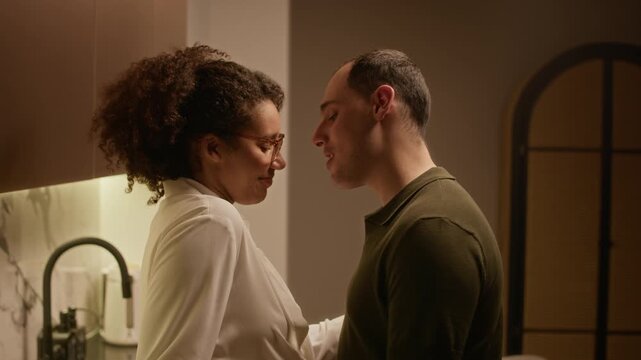 Tilt shot of young man looking at his wife, hugging her while flirting during cooking romantic dinner